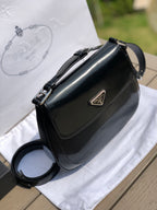 尺寸：19*6*24cm（56980898）PRADA代工廠出品翻蓋腋下包❗️普拉達這款精緻的Prada Cleo手袋重新詮釋品牌標誌性的復古設計。底部和側面獨特的傾斜結構彰顯這款翻蓋手袋簡約的弧形線條，賦予其輕盈柔和的造型風格。 Prada系列別緻的亮面皮革材質頗具現代感與多變風格，慣於創造嶄新的組合與對比效果。琺瑯三角形標誌呈現鮮明的品牌格調。磁扣扣合Prada標誌尼龍襯裡，配上貼布口袋。可延長皮革提把，可將單肩包變成斜背包！