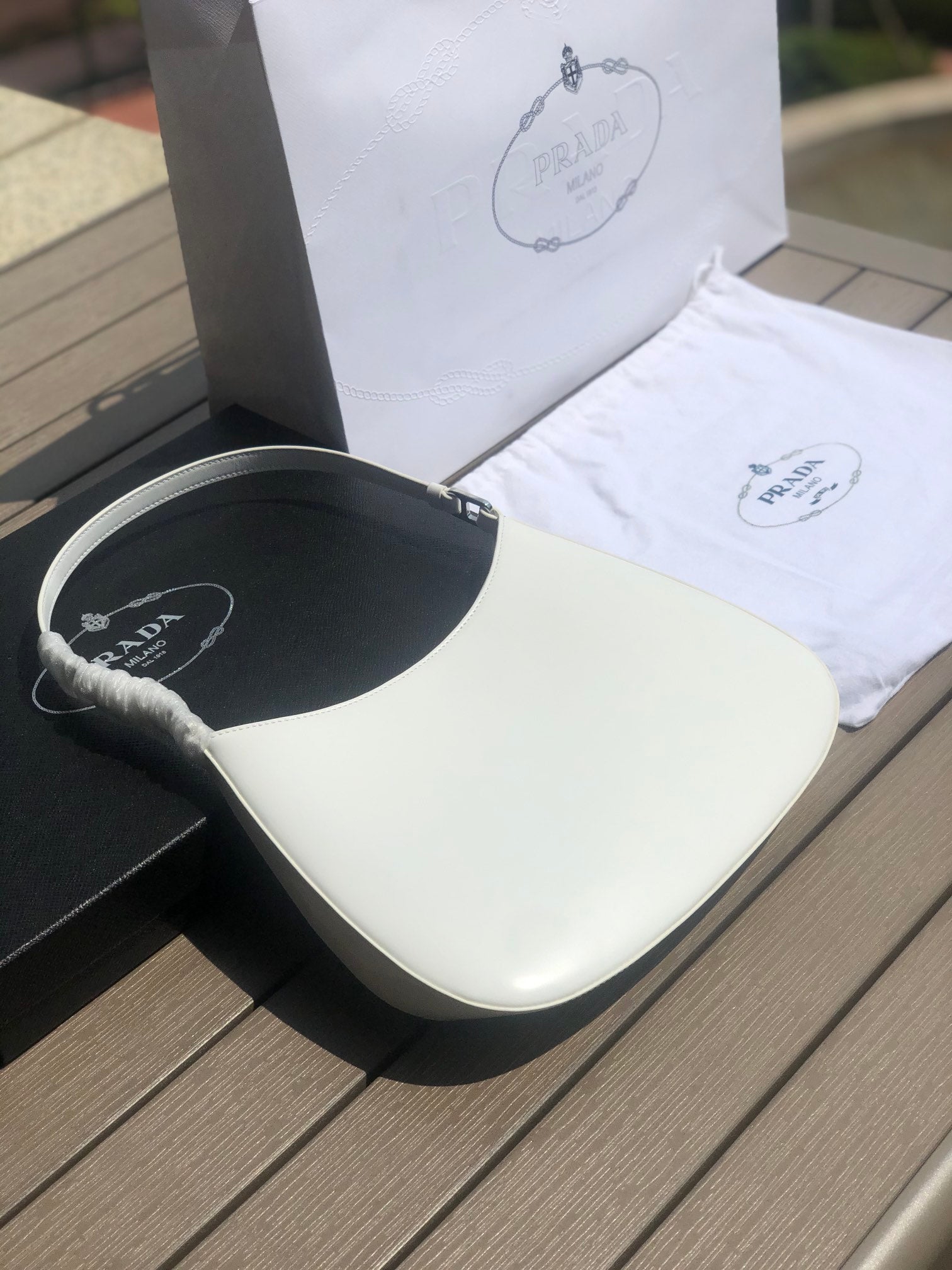 白色❗️尺寸：22*6*27cm（05850898）PRADA代工廠訂單出品腋下包❗️普拉達這款Prada Cleo單肩包重釋1990年代品牌標誌性的設計，頗具精緻格調。單肩包結構別緻，底部和側面漸顯圓潤，彰顯簡約的弧形線條，賦予其新月包風格的柔美輕盈外觀。 Prada系列中的亮面皮革材質現代而百搭，是打造全新組合與對比感的理想之選。三角形琺瑯標誌呈現不凡的品牌格調，亮面皮革材質皮革提手金屬配件，琺瑯三角形金屬徽標，磁扣扣合，Prada徽標尼龍襯裡，配貼布口袋