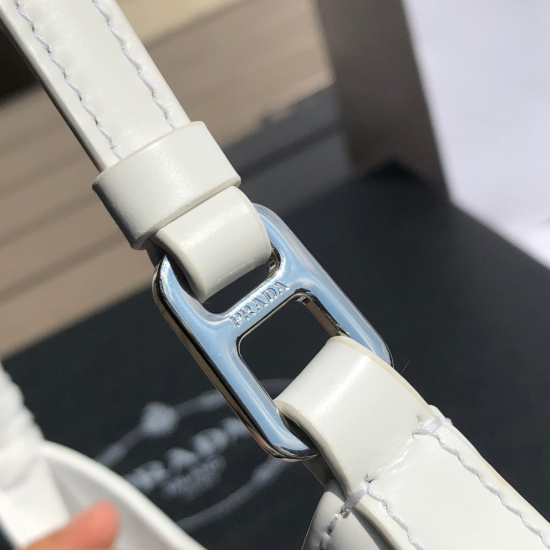 白色❗️尺寸：22*6*27cm（05850898）PRADA代工廠訂單出品腋下包❗️普拉達這款Prada Cleo單肩包重釋1990年代品牌標誌性的設計，頗具精緻格調。單肩包結構別緻，底部和側面漸顯圓潤，彰顯簡約的弧形線條，賦予其新月包風格的柔美輕盈外觀。 Prada系列中的亮面皮革材質現代而百搭，是打造全新組合與對比感的理想之選。三角形琺瑯標誌呈現不凡的品牌格調，亮面皮革材質皮革提手金屬配件，琺瑯三角形金屬徽標，磁扣扣合，Prada徽標尼龍襯裡，配貼布口袋