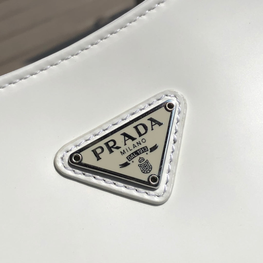 白色❗️尺寸：22*6*27cm（05850898）PRADA代工廠訂單出品腋下包❗️普拉達這款Prada Cleo單肩包重釋1990年代品牌標誌性的設計，頗具精緻格調。單肩包結構別緻，底部和側面漸顯圓潤，彰顯簡約的弧形線條，賦予其新月包風格的柔美輕盈外觀。 Prada系列中的亮面皮革材質現代而百搭，是打造全新組合與對比感的理想之選。三角形琺瑯標誌呈現不凡的品牌格調，亮面皮革材質皮革提手金屬配件，琺瑯三角形金屬徽標，磁扣扣合，Prada徽標尼龍襯裡，配貼布口袋