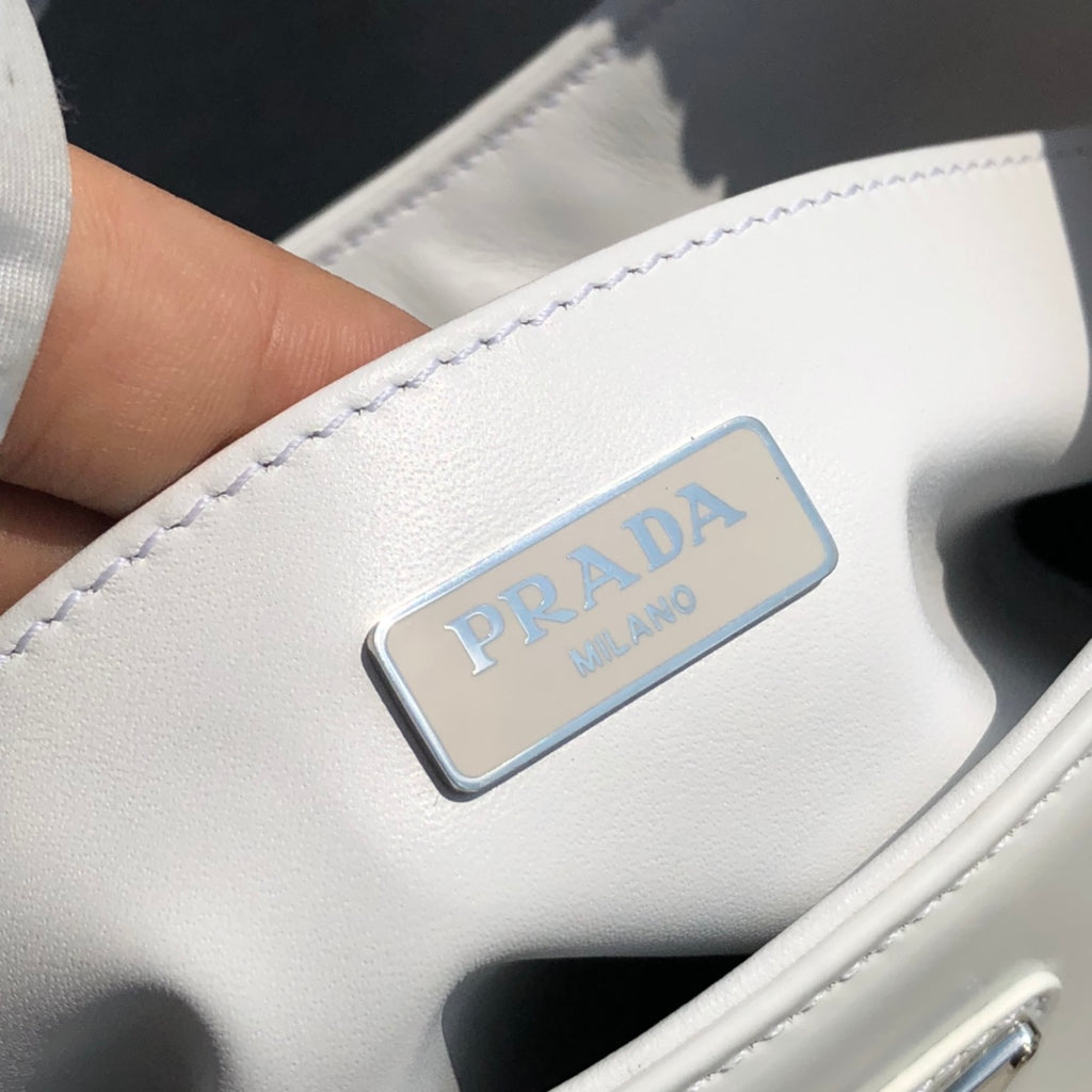 白色❗️尺寸：22*6*27cm（05850898）PRADA代工廠訂單出品腋下包❗️普拉達這款Prada Cleo單肩包重釋1990年代品牌標誌性的設計，頗具精緻格調。單肩包結構別緻，底部和側面漸顯圓潤，彰顯簡約的弧形線條，賦予其新月包風格的柔美輕盈外觀。 Prada系列中的亮面皮革材質現代而百搭，是打造全新組合與對比感的理想之選。三角形琺瑯標誌呈現不凡的品牌格調，亮面皮革材質皮革提手金屬配件，琺瑯三角形金屬徽標，磁扣扣合，Prada徽標尼龍襯裡，配貼布口袋