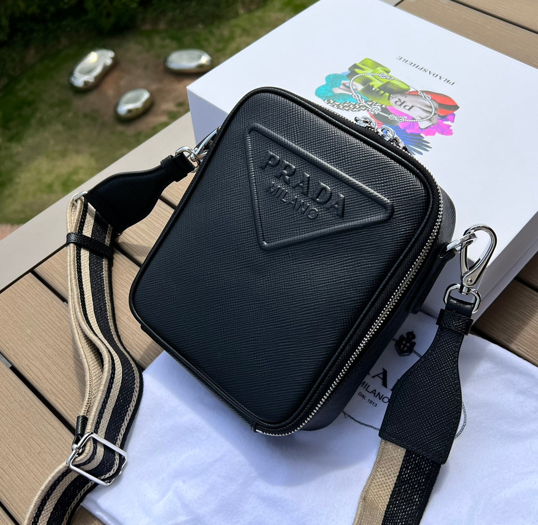尺寸:19×16×5.5cm（581150898） PRADA通路資源特供訂單❗️Saffiano皮革壓花標誌手機包，採用普拉達標誌性的Saffiano 皮革，呈現別緻的交叉平行線陰影紋理和塗蠟飾面。 Prada 富有像徵意義的三角形標誌化身大幅壓花細節鋪陳於正面。背面塗琺瑯金屬三角形標誌，拉鍊開合，RE-Nylon 再生尼龍襯裡，可拆卸調價刺繡織帶肩帶