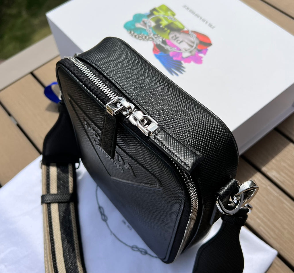 尺寸:19×16×5.5cm（581150898） PRADA通路資源特供訂單❗️Saffiano皮革壓花標誌手機包，採用普拉達標誌性的Saffiano 皮革，呈現別緻的交叉平行線陰影紋理和塗蠟飾面。 Prada 富有像徵意義的三角形標誌化身大幅壓花細節鋪陳於正面。背面塗琺瑯金屬三角形標誌，拉鍊開合，RE-Nylon 再生尼龍襯裡，可拆卸調價刺繡織帶肩帶