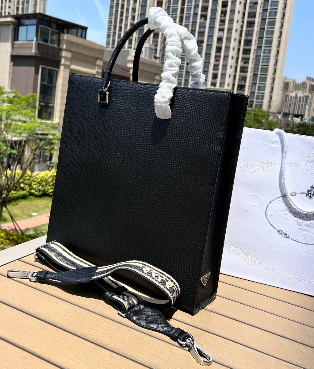 尺寸:37×35×7cm（111450898） PRADA通路資源特供訂單❗️男士托特包，這款時尚簡約的托特包取材品牌標誌性的Saffiano 皮革，呈現別緻的交叉平行線陰影紋理和塗蠟飾面。 Prada 富有像徵意義的三角形標誌化身大幅壓花細節，re-Nylon 再生尼龍襯裡，可拆卸調整刺繡織帶、皮革手柄！風格中性實用，整體設計簡約大方，搭配商務穿搭更有質感