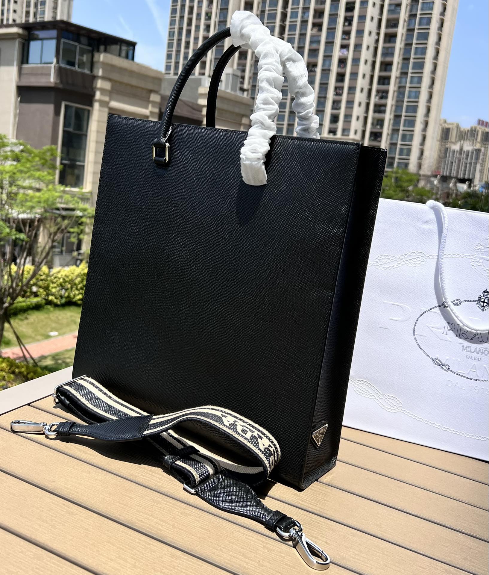 尺寸:37×35×7cm（111450898） PRADA通路資源特供訂單❗️男士托特包，這款時尚簡約的托特包取材品牌標誌性的Saffiano 皮革，呈現別緻的交叉平行線陰影紋理和塗蠟飾面。 Prada 富有像徵意義的三角形標誌化身大幅壓花細節，re-Nylon 再生尼龍襯裡，可拆卸調整刺繡織帶、皮革手柄！風格中性實用，整體設計簡約大方，搭配商務穿搭更有質感
