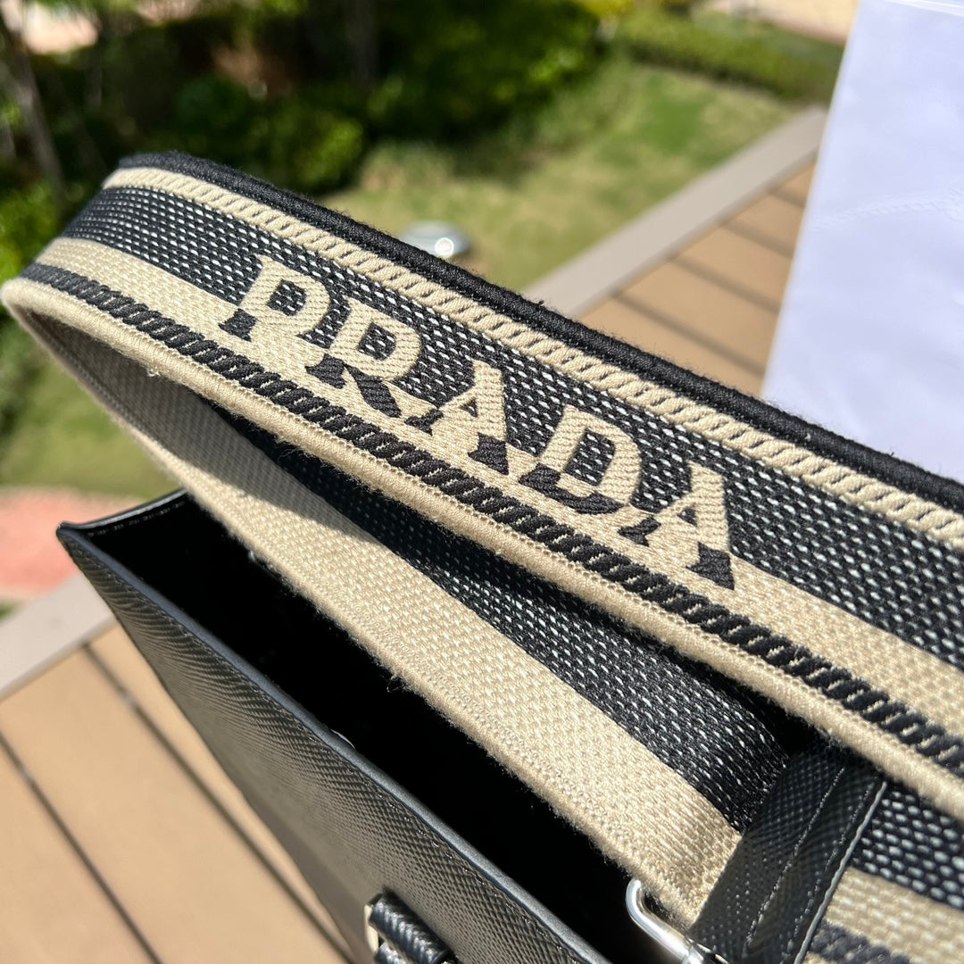 尺寸:37×35×7cm（111450898） PRADA通路資源特供訂單❗️男士托特包，這款時尚簡約的托特包取材品牌標誌性的Saffiano 皮革，呈現別緻的交叉平行線陰影紋理和塗蠟飾面。 Prada 富有像徵意義的三角形標誌化身大幅壓花細節，re-Nylon 再生尼龍襯裡，可拆卸調整刺繡織帶、皮革手柄！風格中性實用，整體設計簡約大方，搭配商務穿搭更有質感