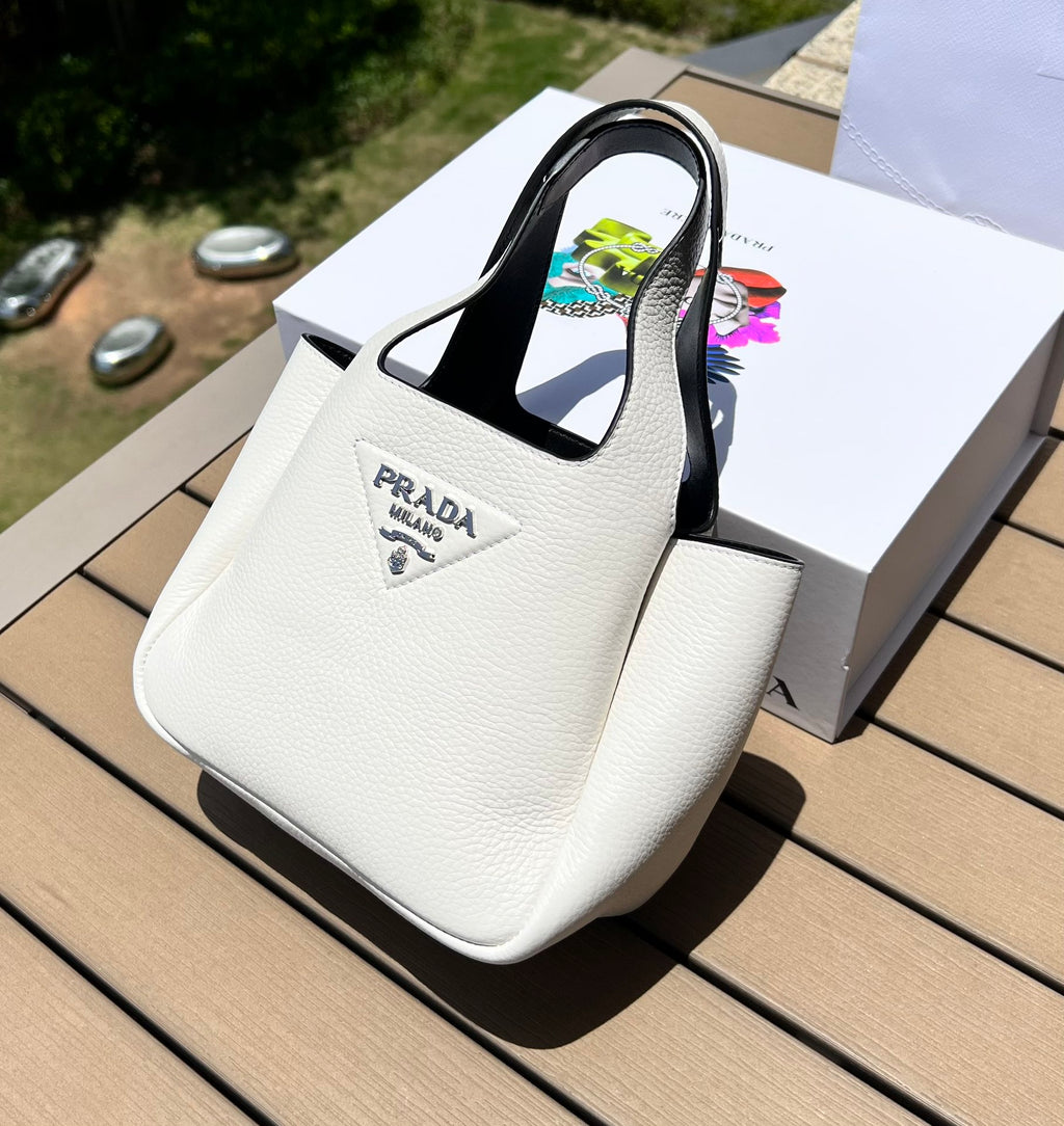 尺寸:18×15.5×10cm（56980898） PRADA通路資源特供菜籃❗️反向針跡彰顯這款手提包柔和圓潤的輪廓。包身飾以縫線工藝勾勒的三角形，藉由新穎設計重塑標誌性元素。 Prada 金屬刻字標誌點綴於中央，光澤閃耀，皮革手提，正面金屬刻字徽標，磁扣開合，軟羊革襯裡，配有三個隔層。通勤百搭！