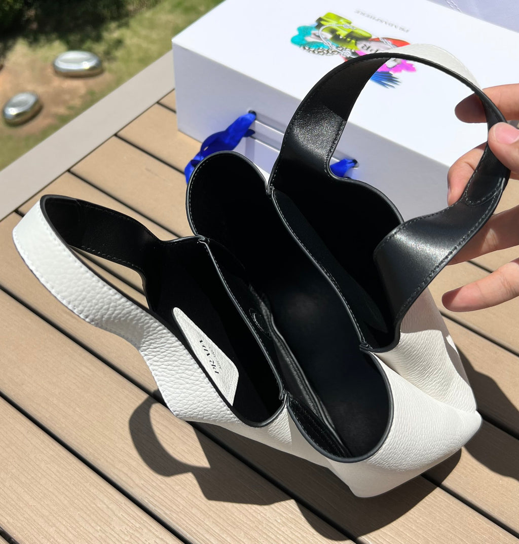 尺寸:18×15.5×10cm（56980898） PRADA通路資源特供菜籃❗️反向針跡彰顯這款手提包柔和圓潤的輪廓。包身飾以縫線工藝勾勒的三角形，藉由新穎設計重塑標誌性元素。 Prada 金屬刻字標誌點綴於中央，光澤閃耀，皮革手提，正面金屬刻字徽標，磁扣開合，軟羊革襯裡，配有三個隔層。通勤百搭！
