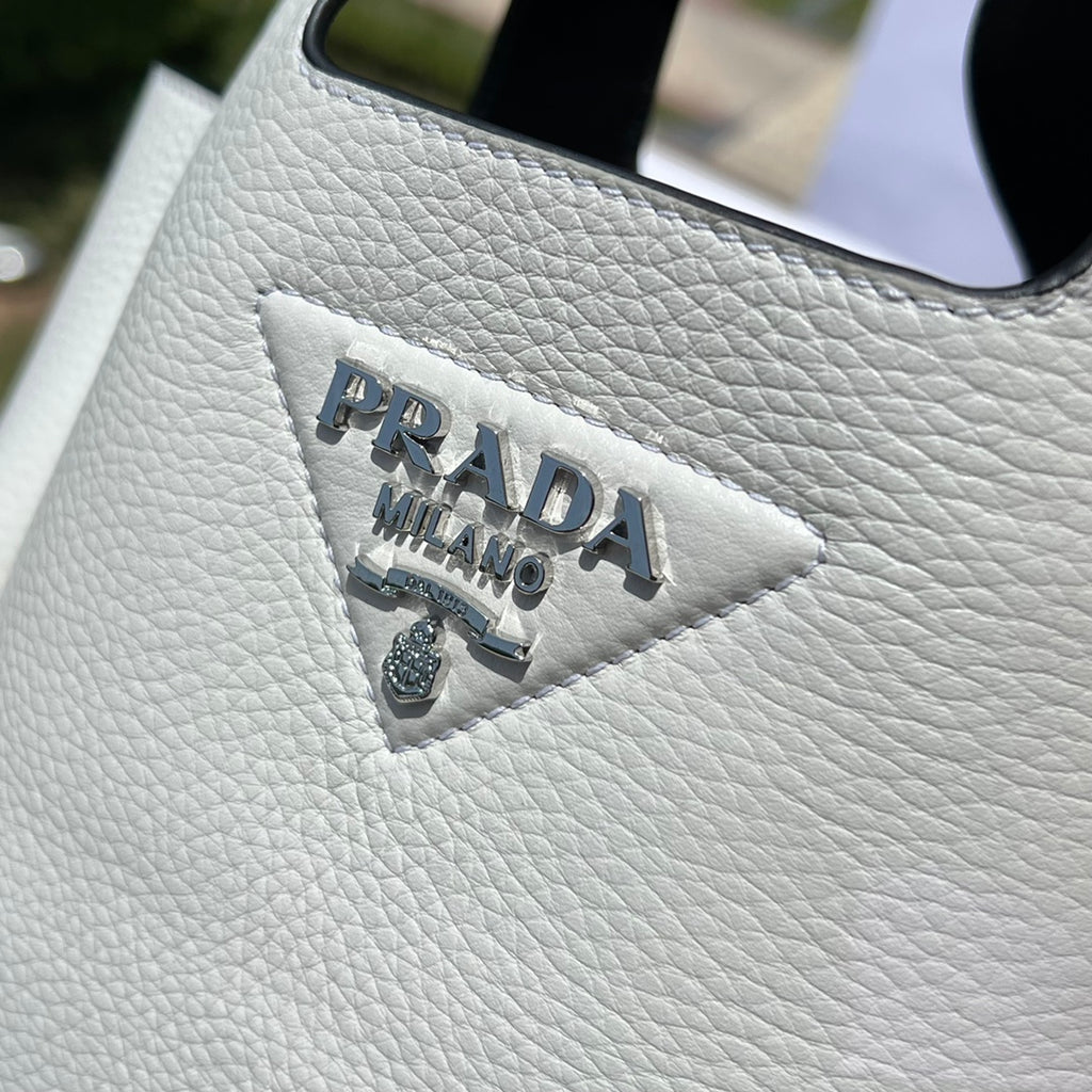尺寸:18×15.5×10cm（56980898） PRADA通路資源特供菜籃❗️反向針跡彰顯這款手提包柔和圓潤的輪廓。包身飾以縫線工藝勾勒的三角形，藉由新穎設計重塑標誌性元素。 Prada 金屬刻字標誌點綴於中央，光澤閃耀，皮革手提，正面金屬刻字徽標，磁扣開合，軟羊革襯裡，配有三個隔層。通勤百搭！